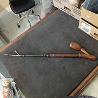 Full view of the wooden German ceremonial pipe laid out on a dark fabric surface, highlighting its length and curved wooden bowl.