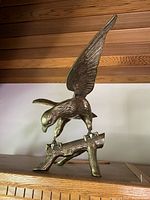 Side view of brass eagle statue perched on a textured branch, showing detailed feathers and form.