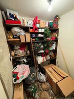 Full view of small closet packed with boxes, Christmas wreaths, garlands, bags, and miscellaneous items on wooden shelves and floor.