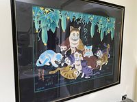 Framed cat artwork showing multiple colorful cats under hanging green fruit and leaves, in a dark background.