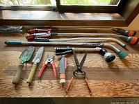 Top-down view of all garden equipment laid on wooden floor, showing hand trowels, pruning shears, garden scissors, spray nozzle, and watering wands.
