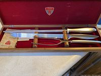 Full view of Gerber carving set inside wooden box with red velvet lining showing knife, fork, sharpening steel, and Gerber logo inside lid.