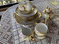 Wide shot showing all items in set including plates, teacups stacked on small plates, creamer, sugar bowl, large serving tray on lace tablecloth.