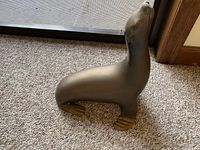 Side view of the large brass seal figurine on carpet showing the overall shape, posture, and brass flippers.