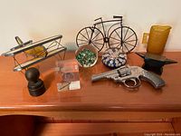Lot overview including metal and wood biplane model, wire bicycle sculpture, glass paperweight, toy gun, amber glass pitcher, small anvil, black ball on stand