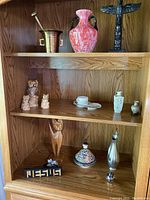 Full view of wooden display cabinet with assorted decorative items on three shelves showing the collection, including vase, owl figurines, cat sculpture, and other items.