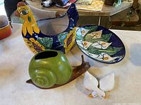 Group photo showing hen dish, snail figurine, ceramic plate, and bird figurines on table.