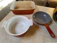 Three Descoware-style pots and pans on light countertop: rectangular casserole dish, round pot, and frying pan.
