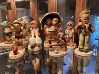 Seven Hummel figurines displayed on glass shelf