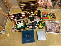 Lot overview showing multiple vintage games including backgammon board, Tripoley game, chess/checkers pieces, jigsaw puzzle, and Trivial Pursuit editions.