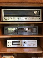 Three components stacked on woodgrain shelf: silver Pioneer receiver, black Pioneer cassette deck, silver Akai deck
