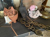Lot overview showing ceramic cat pot, brass badges, brass kettle, plush bear vase with flowers on fireplace hearth.
