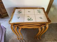 Set of three wooden nesting tables stacked, showing tile tops with floral illustrations