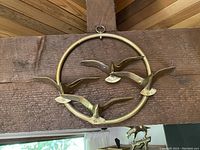 Front view of the solid brass bird wall hanging mounted on wooden beam, showing three birds in flight inside a circular frame.