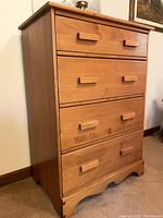 Front angled view of the solid wood chest of drawers showing four drawers with rectangular wooden handles and scalloped base.