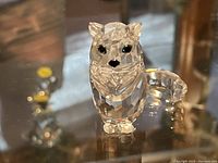 Front view of the clear multi-faceted crystal fox figurine with black eyes and nose on a glass surface.