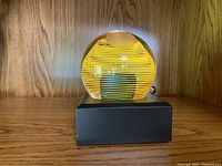 Front view of the spherical vintage glass paperweight showing the yellow spiral pattern and frosted dome detail on black display base.