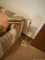 Full view of vintage brass floor lamp showing adjustable arm and cylindrical shade next to a striped couch.