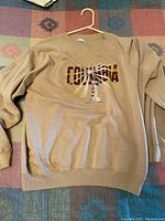 Full view of tan Columbia sweatshirt laid flat, showing front design and overall condition.