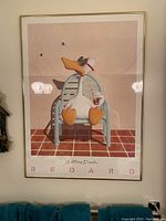 Full view of the framed Sitting Duck poster on a wall with two blue towels below.