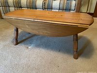 Side view of vintage solid wood drop leaf side table with one leaf down, showing turned legs and wood grain surface with minor wear.