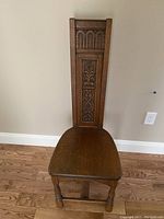 Full view of antique wooden chair showing tall backpack with carved designs and plain wooden seat.