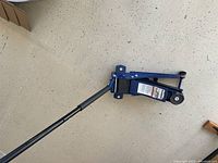 Full view of the blue Stronghold 2-1/2 ton service car jack with extended black handle and wheels visible.