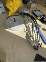 Overall view of the folded umbrella fabric, blue protective sleeve, curved black metal poles, and round concrete base with metal holder pipe.
