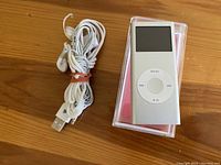 Apple iPod Nano 2GB in clear plastic case with bundled earbuds and USB cable on wooden surface.