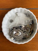 Photo showing miscellaneous vintage jewelry items in white dish, includes rhinestone pendant, mixed bead bracelets, chains, and assorted small jewelry pieces.