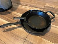Two cast iron pans stacked on the floor showing general condition and size difference.