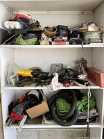 Three-tier white shelving unit filled with various items including golf ball boxes, tools, hoses, ropes and sports gear