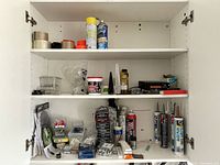 Photo of cabinet shelves holding tapes, spray cans, containers and hardware items showing general lot contents.