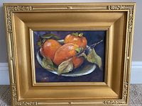 Framed oil painting showing the full artwork with a gold ornate wooden frame and persimmons on a plate.