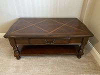 Solid wood coffee table with turned legs, drawer on the front, and a lower shelf beneath. Visible wear and vintage character.