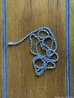 Full view of the silver twisted rope necklace laid out on a wooden surface.