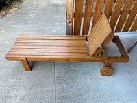 Side view of wooden patio lounger showing overall design, slatted seat, and wheels.