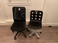 Front view of two office chairs side by side; one black mesh back with cushioned seat, one black plastic seat and backrest with circular holes on caster wheels.