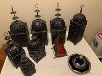 Seven black metal Arabic-style lanterns with intricate cut-out patterns, small metal red interior display holder, and blue silver dish.
