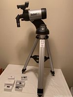 Full view of the Bushnell North Star telescope mounted on the motorized aluminum tripod with several eyepieces in original boxes on table.