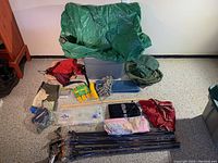 Overview of lot including green tarp, flys in assorted colors, tent pegs with container, rope, poles, compression bags