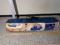 Blue carrying bag with label showing brand Broadstone and series Tillebrook, indicating it's a 3-person dome tent. Product info and setup illustration visible.