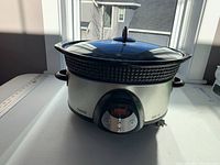 Front view of large Crockpot slow cooker with stainless steel and black plastic design, glass lid on top, showing control panel with display and buttons.