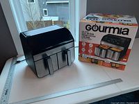 Black Gourmia dual basket air fryer with digital interface alongside its original box showing product details.