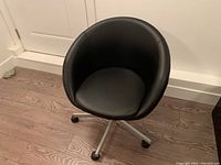Front view of black faux leather swivel office chair with rounded seat and backrest on metal five-wheel base