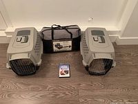 Two closed plastic pet crates with a soft fabric pet trolley bag between them and crate training DVD in front.