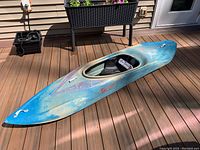 Blue Savage Design white water kayak on wooden deck, showing front and side profile with faded paint and logo.