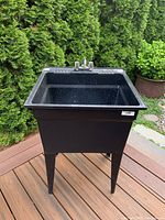 Front view of a black plastic utility sink with faucet attached on top and four supporting legs.