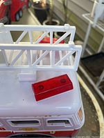 Close up of detached red ladder light on top of white fire truck half showing ladder rails