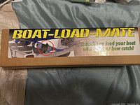Top of the box showing the brand name Boat-Load-Mate and a photo of the product installed on a boat trailer's bow catch.